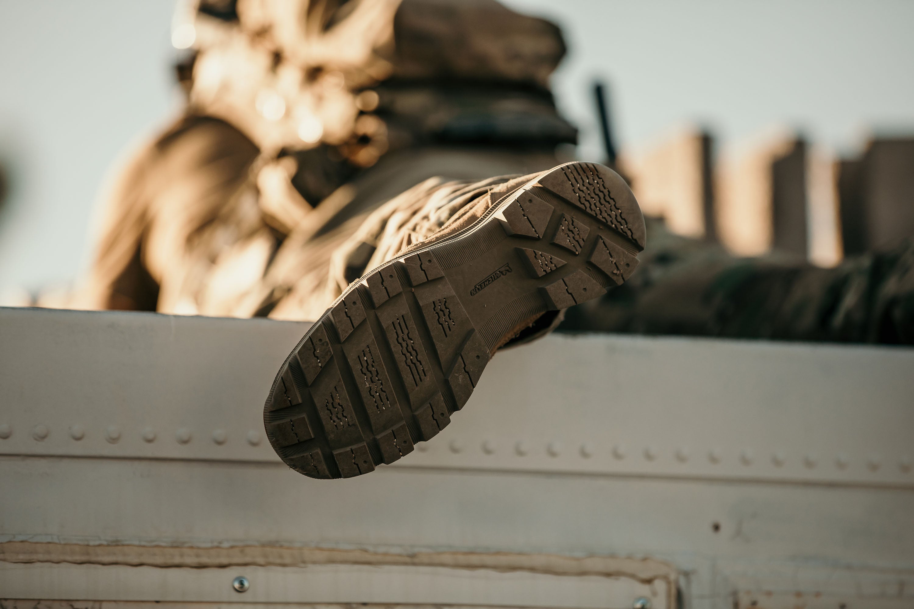 Coyote brown tactical boot with a Soles by Michelin tread on a military vehicle with a soldier in the background